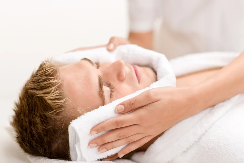 A man examines his skin closely in the mirror, showing signs that may benefit from fractional laser therapy.