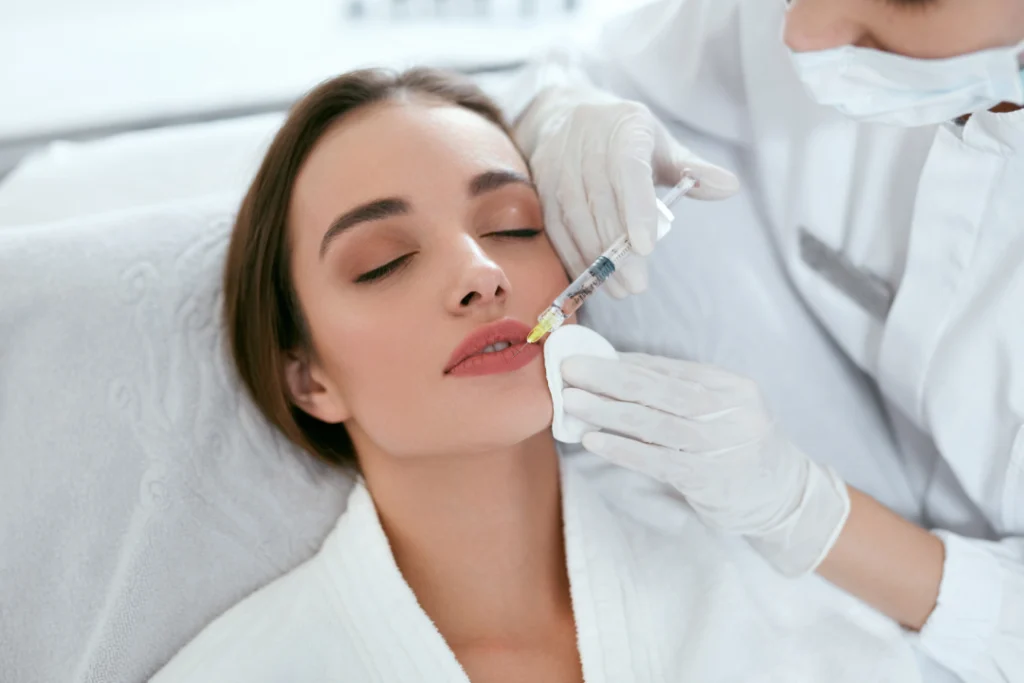 A woman receiving a lip enhancement injection at a medspa by a professional wearing gloves and a face mask.